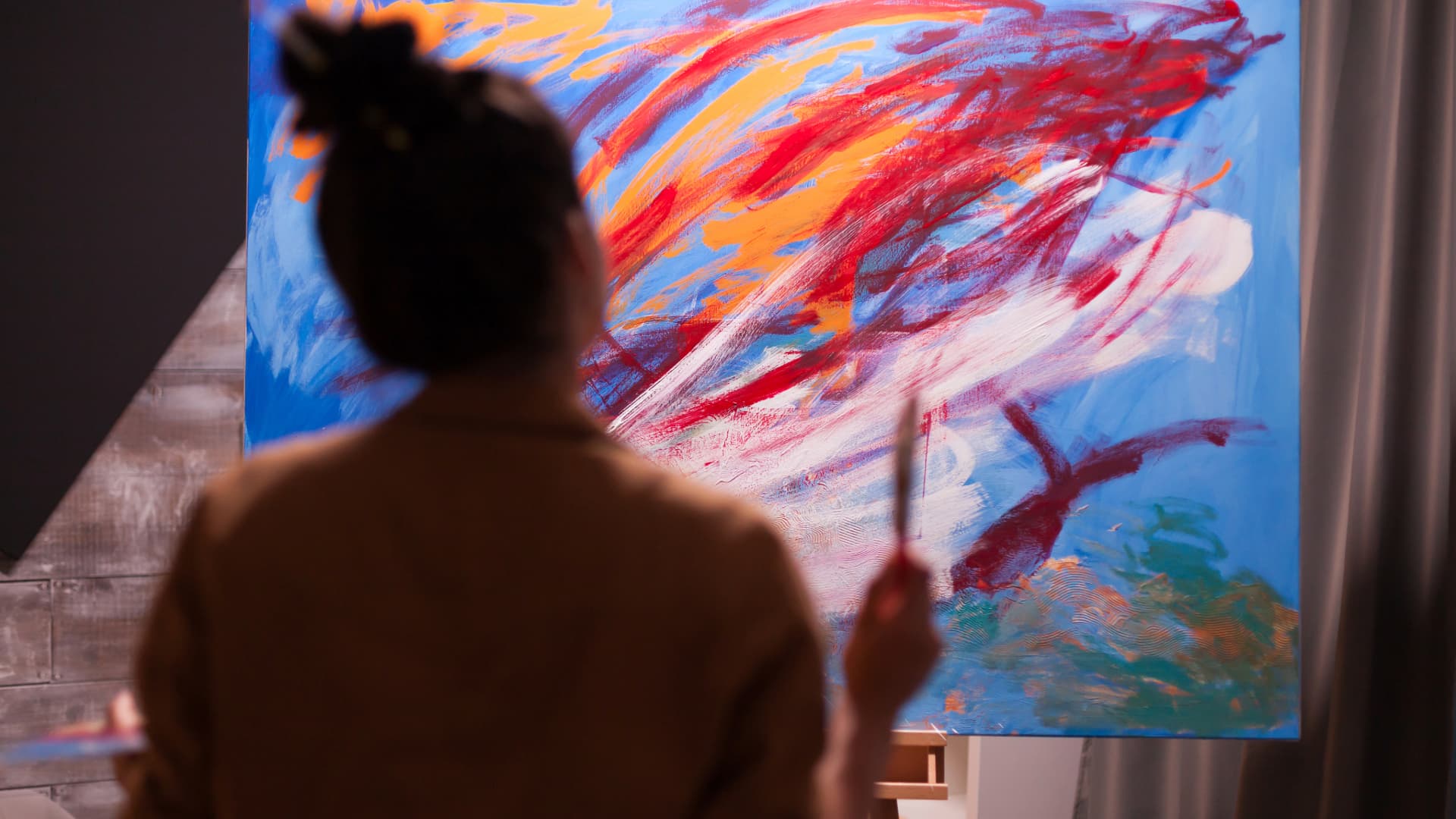 A person observing a painting they are working on, symbolizing the relationship between personal identity and artistic expression.